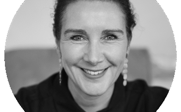 Black and white portrait of Rebecca Pearce, a woman with dark hair pulled back, wearing earrings and a collared shirt, smiling warmly while looking directly at the camera.