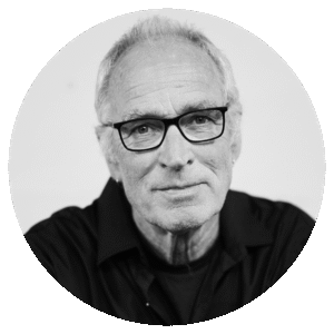Black and white portrait of David McLean, an older man with short, light hair, wearing glasses and a dark shirt, looking directly at the camera with a slight smile. The background is plain and uncluttered.