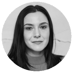 Black and white portrait of a woman with long dark hair, a nose ring, and a slight smile, looking directly at the camera, set against a plain light background.