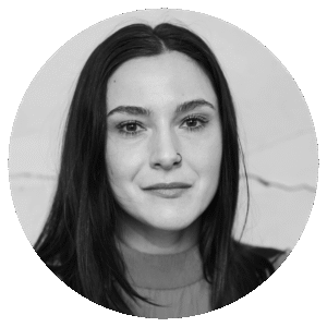 Black and white portrait of a woman with long dark hair, a nose ring, and a slight smile, looking directly at the camera, set against a plain light background.