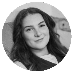 Ren Williams, a young woman with long, wavy hair, smiles softly while sitting on a patterned chair. The black and white image is framed in a circular crop.