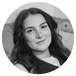 Ren Williams, a young woman with long, wavy hair, smiles softly while sitting on a patterned chair. The black and white image is framed in a circular crop.
