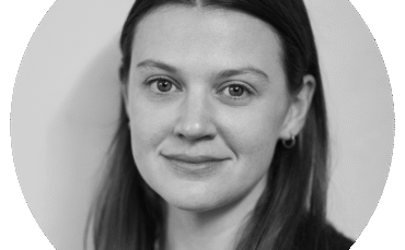Black and white portrait of a young woman with straight, dark hair, wearing small hoop earrings and a light-colored top, looking directly at the camera with a neutral expression.